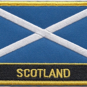 May include: A blue and white embroidered patch with a white cross on a blue background. The patch has a black border and a yellow border around the outside. The text "SCOTLAND" is written in yellow letters on a black background.
