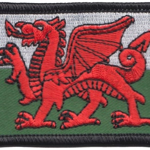 May include: A red dragon embroidered on a white and green flag. The flag is surrounded by a black border.