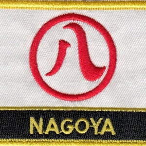 May include: A white and black embroidered patch with a red circle containing a stylized red letter "A" and the word "NAGOYA" in yellow letters.