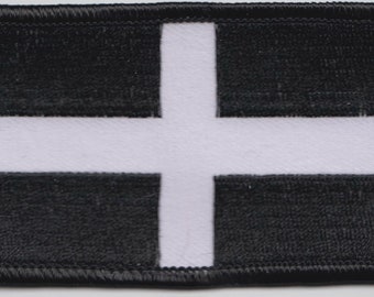May include: A black and white patch with a white cross in the center. The patch has a black border.