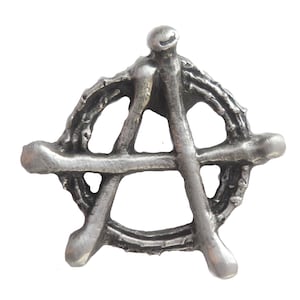 May include: A silver metal pin in the shape of an anarchy symbol. The symbol is made of five points that form a star.