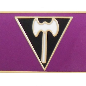 May include: A purple and black enamel pin with a white axe in a triangle shape.