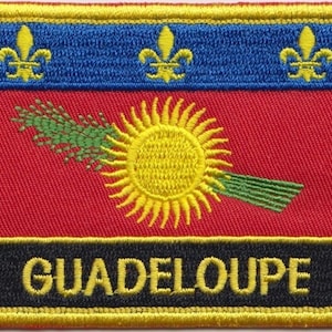 Puede incluir: Un parche bordado en amarillo, rojo, azul y negro con el texto "GUADELOUPE" en amarillo. El parche presenta un sol estilizado con rayos y una espiga de trigo verde.
