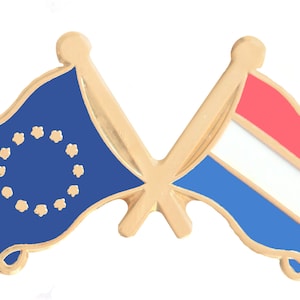 Puede incluir: Pin de color dorado con dos banderas cruzadas. La bandera de la izquierda es azul con un círculo de estrellas doradas, que representa la Unión Europea. La bandera de la derecha es roja, blanca y azul, que representa a los Países Bajos.
