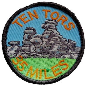 May include: A round, blue and green embroidered patch with the text "TEN TORS 35 MILES" in orange thread. The patch features a gray embroidered image of a rock formation.