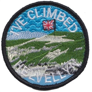 May include: A blue and green embroidered patch with the text "I Climbed Snowdon" and a small Union Jack flag. The patch is circular and has a black border.