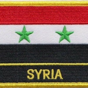 Op de afbeelding: Een rechthoekige geborduurde patch met een rood-wit-zwarte vlag met twee groene sterren. De vlag is omgeven door een gele rand. De tekst "SYRIA" staat in gele letters op een zwarte achtergrond aan de onderkant van de patch.