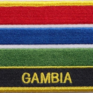 Könnte beinhalten: Ein gestickter Aufnäher mit den Farben der gambischen Flagge, rot, blau, weiß, grün und schwarz, mit dem Wort "GAMBIA" in gelben Buchstaben.