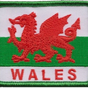 Könnte beinhalten: Gestickter Aufnäher mit der walisischen Flagge. Das Design zeigt einen roten Drachen auf weißem Grund, einen grünen Streifen und das Wort „WALES“ in Rot. Der Aufnäher hat einen grün gestickten Rand.