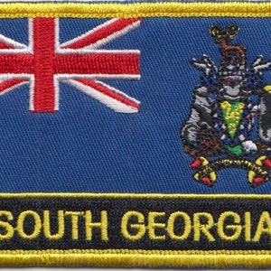 May include: A blue embroidered patch with a Union Jack flag on the left and a coat of arms on the right. The text "SOUTH GEORGIA" is printed in yellow on a black background at the bottom of the patch.
