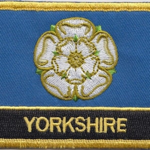 May include: A blue and gold embroidered patch featuring a white rose and the word "YORKSHIRE" in gold lettering.