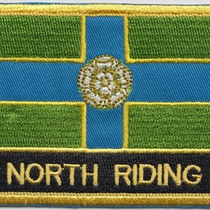 Op de afbeelding: Een geborduurde patch in groen, blauw en wit met een gouden rand. De patch heeft een witte roos met een gouden centrum en de tekst "NORTH RIDING" in gouden letters op een zwarte achtergrond.