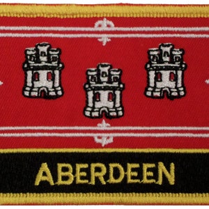 Puede incluir: Un parche bordado rojo con tres castillos blancos y la palabra "ABERDEEN" en letras doradas sobre fondo negro.