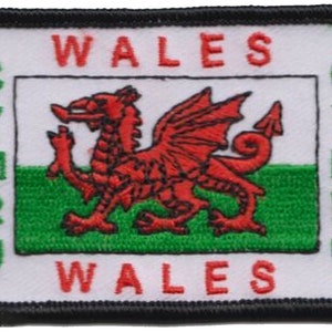 May include: A white embroidered patch with a red dragon on a green and white background. The patch says "WALES" in red letters at the top and bottom and "CYMRU" in white letters on the sides.