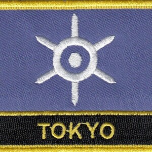 May include: A blue and gold embroidered patch with a white stylized sunburst design and the word "TOKYO" in black lettering.