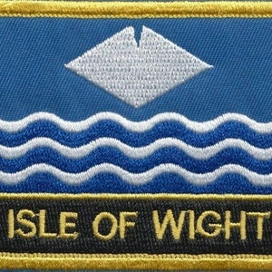 May include: A blue and white embroidered patch with the text "ISLE OF WIGHT" in yellow lettering. The patch features a white stylized ship's sail and wavy lines representing water.