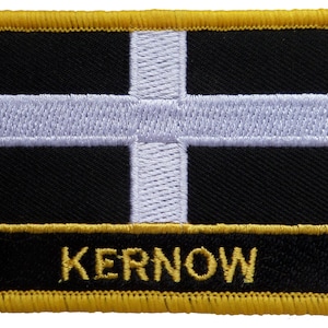 May include: A black and white embroidered patch with a white cross on a black background. The patch has a yellow border and the word "KERNOW" is embroidered in yellow on a black background at the bottom.