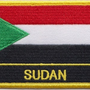 Könnte beinhalten: Ein gestickter Aufnäher mit der Flagge des Sudan. Die Flagge ist grün, schwarz, weiß und rot mit einem grünen Dreieck in der oberen linken Ecke. Das Wort "SUDAN" ist in Gelb am unteren Rand des Aufnähers gestickt.