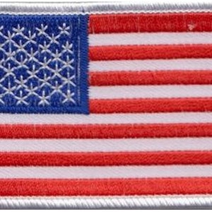 May include: A small embroidered American flag patch with white stitching on a white background. The flag is surrounded by a white border.