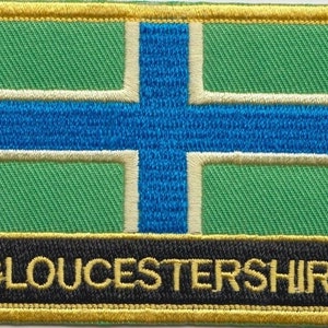 Op de afbeelding: Een geborduurde patch met de vlag van Gloucestershire, met de tekst "GLOUCESTERSHIRE" in zwarte letters op een zwarte achtergrond.
