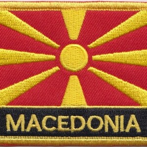 Puede incluir: Parche bordado con la bandera de Macedonia del Norte. La bandera presenta un campo rojo con un sol amarillo de ocho rayos. El parche tiene un borde negro con la palabra "MACEDONIA" en letras amarillas.