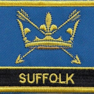 May include: A blue embroidered patch featuring a gold crown and two crossed arrows. The text "SUFFOLK" is embroidered in gold on a black background.