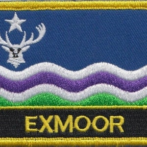May include: An embroidered patch featuring a white deer and a star on a blue background. The patch has a black border with the word "EXMOOR" in yellow letters. The design also includes green and purple waves.