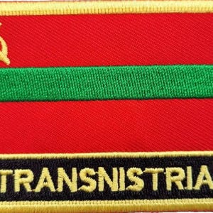 May include: An embroidered patch featuring a red, green and black design with a gold border and the word "TRANSNISTRIA" in yellow lettering.
