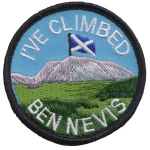 Op de afbeelding: Een ronde, blauw-groene geborduurde patch met de tekst "I've Climbed Ben Nevis" en een Schotse vlag op de top van een berg.