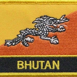 May include: A yellow and orange embroidered patch featuring a white dragon and the word "BHUTAN" in yellow lettering on a black background.