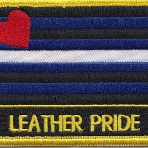 May include: A black, blue and white leather pride flag with a red heart in the top left corner. The flag has the text "LEATHER PRIDE" at the bottom.