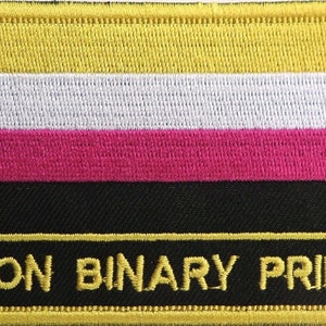 Könnte beinhalten: Ein gestickter Aufnäher in Gelb, Weiß, Rosa und Schwarz mit dem Text "NON BINARY PRIDE" in Gelb.