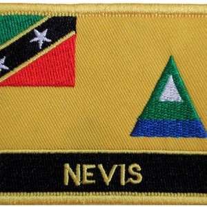 May include: A yellow fabric patch with the flag of Saint Kitts and Nevis on the left side and a green triangle with a white triangle inside on the right side. The words "NEVIS" are printed in yellow on a black background at the bottom of the patch.