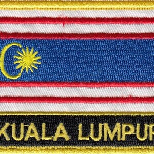 Könnte beinhalten: Ein gestickter Aufnäher mit der malaysischen Flagge in Gelb, Rot und Blau, mit dem Text "KUALA LUMPUR" in gelben Buchstaben auf schwarzem Hintergrund.