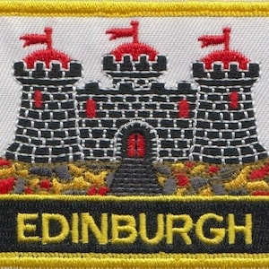 Op de afbeelding: Geborduurde patch met een zwart-wit kasteel met rode accenten op een witte achtergrond. Het kasteel is omgeven door een gele rand en het woord "EDINBURGH" staat in geel op een zwarte achtergrond.