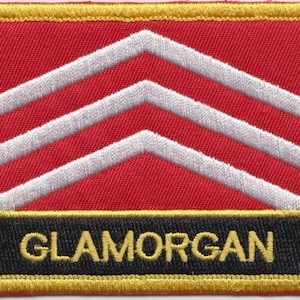 Könnte beinhalten: Roter und weißer gestickter Aufnäher mit drei weißen Chevron und dem Wort "GLAMORGAN" in gelben Buchstaben auf schwarzem Hintergrund.