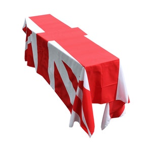 May include: A red and white tablecloth with a geometric pattern. The tablecloth is draped over a table and the edges are hanging down.