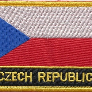 May include: Embroidered patch featuring the Czech Republic flag. The flag is white with a blue triangle in the top left corner and a red horizontal stripe below. The patch has a black border with gold stitching and the text "CZECH REPUBLIC" in gold lettering.