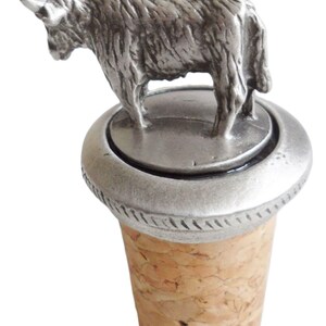 May include: A silver bottle stopper with a detailed pewter Highland Cow figurine on top. The stopper is made of cork and has a silver base.