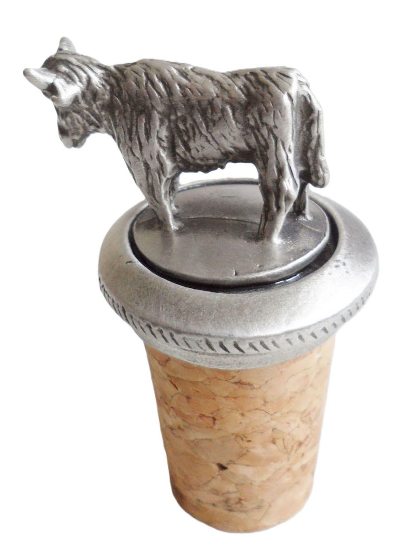 May include: A silver bottle stopper with a detailed pewter Highland Cow figurine on top. The stopper is made of cork and has a silver base.