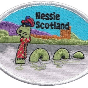 May include: An embroidered patch featuring a cartoon Nessie, the Loch Ness Monster, wearing a red and green plaid scarf and a blue and red hat. The patch is oval shaped with a white border and a blue background. The text "Nessie Scotland" is written in black above the monster.