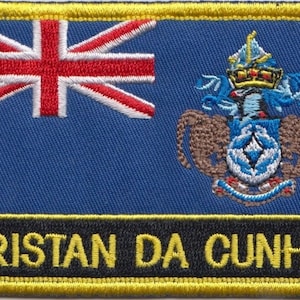 May include: Embroidered patch featuring the flag of Tristan da Cunha, a British Overseas Territory. The design includes the Union Jack, a coat of arms, and the text "TRISTAN DA CUNHA" in yellow lettering on a black background, with a yellow border.