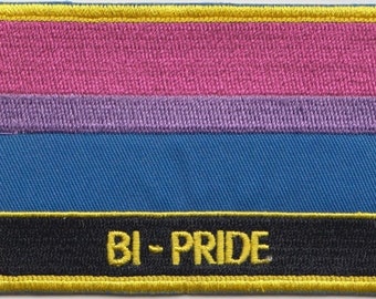 May include: A bisexual pride flag patch with a pink, lavender, blue, and black striped design. The patch has a yellow border and the text "BI-PRIDE" in yellow lettering.