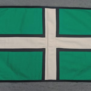 Peut inclure: Un drapeau rectangulaire composé d'un champ vert divisé par une croix horizontale et une croix verticale blanches, bordées de fines lignes noires. Le côté gauche présente une bande en toile blanche avec deux œillets et une boucle.