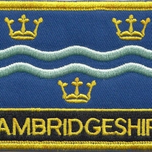 Op de afbeelding: Een blauwe en gouden geborduurde patch met de tekst "CAMBRIDGESHIRE" en drie gouden kronen. De patch heeft een gele rand.