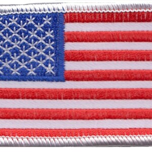 Könnte beinhalten: Ein kleiner gestickter amerikanischer Flaggen-Patch mit weißen Nähten an den Rändern. Die Flagge ist rot, weiß und blau mit 13 horizontalen Streifen und 50 weißen Sternen auf einem blauen Feld.