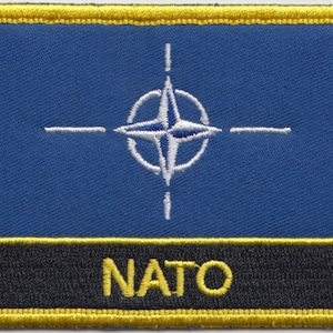 May include: A blue patch with a white compass rose and the word "NATO" in yellow letters.
