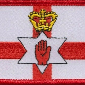 Puede incluir: Un parche blanco con una cruz roja y una mano roja dentro de una estrella de seis puntas. Una corona dorada se encuentra sobre la estrella. El parche tiene un borde rojo.