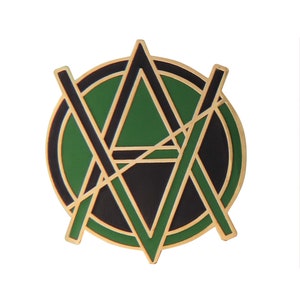 May include: A gold-colored pin with a green and black geometric design. The design features a circle with a triangle inside, and lines intersecting the circle and triangle.