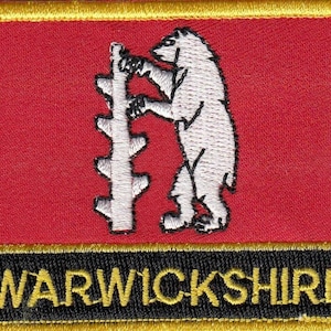 Könnte beinhalten: Ein roter gestickter Aufnäher mit einem weißen Bären, der einen Baum hinaufklettert, und dem Text "WARWICKSHIRE" in gelben Buchstaben auf schwarzem Hintergrund.